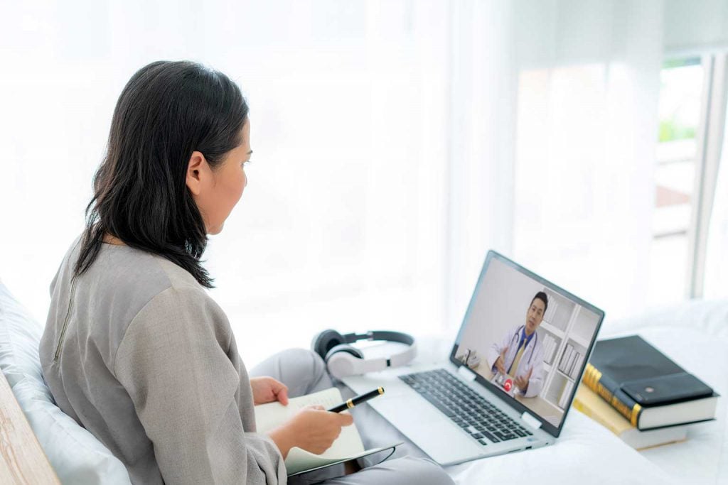 A person sitting at a desk with a laptop, engaged in a video call with a healthcare provider.